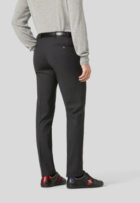 Pantaloni neri con una vestibilità sartoriale, caratterizzati da una texture elegante e un sottile dettaglio della tasca posteriore. Abbinati a sneakers nere con accenti colorati.