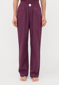 Pantalons ample à taille élastique d'une couleur bordeaux profond. Fabriqués en tissu lisse, avec deux poches latérales et une coupe décontractée.