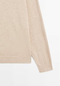 Maglione beige a maglia con maniche lunghe, polsini a coste e una texture liscia. Presenta un collo rotondo e una vestibilità morbida.