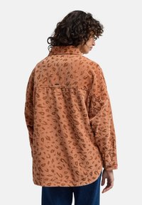 Camicia in corduroy color ruggine con motivo leopardato, dotata di colletto, maniche lunghe e orlo curvo. Include un piccolo etichetta del marchio.