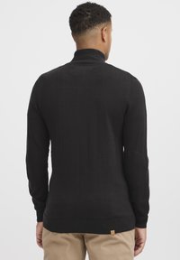 Sort strikket sweater med høj krave, ribbede manchetter og kant, samt albuepatches. Stoffet er glat med en subtil tekstur.