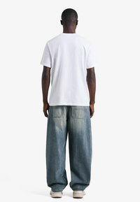 Vitt t-shirt i bomull kombinerad med ljusblå, löst sittande jeans i denim med bakfickor och blekta detaljer. Skor i beige.