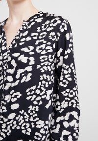 Czarna bluzka z białym abstrakcyjnym nadrukiem zwierzęcym, wykonana z lekkiego materiału, z dekoltem w kształcie litery V i długimi rękawami w luźnym kroju.