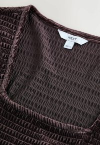 Burgundi színű textúrázott anyagú felső négyzet alakú dekoltázzsal és összegyűrt részletekkel. Címkén a "NEXT" márkanevének és ápolási információinak megjelenítése.