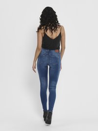 Jeans de mezclilla azul delgados con un lavado desgastado, cintura alta y costuras reforzadas. Combinados con una blusa sin mangas negra y botas de tacón negras.