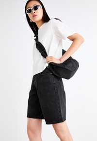 Black denim shorts and a white t-shirt paired with a black crossbody bag. Sunglasses with silver accents complete the look.