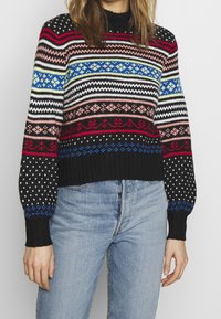 Färgglad stickad tröja med svart bas, med horisontella ränder i röd, rosa, blå och vit, samt ribbade ärmar och nederkant.