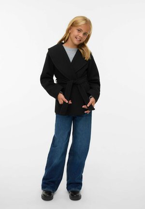 Zwarte wikkeljas met brede kraag, ceintuurd taille en een losse pasvorm, gecombineerd met blauwe wijde jeans en zwarte schoenen. Soepele stoffen textuur.