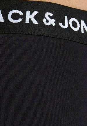 Czarny materiałowy pas z białym logo "JACK & JONES" na czarnym ubraniu, pokazujący teksturę i szczegóły szwów.