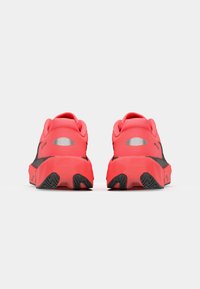 Des chaussures de sport rouges et noires présentent un dessus texturé avec un col rembourré, un talon renforcé, et une semelle angulaire avec un motif de bande de roulement en zigzag.