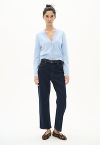 Cardigan azzurro chiaro con scollo a V e chiusura a bottoni, abbinato a jeans a gamba dritta blu scuro e scarpe slip-on con stampa leopardata.