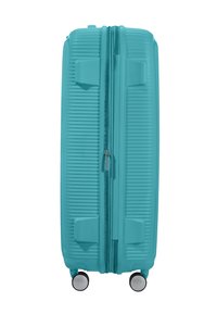 Valise rigide turquoise avec texture striée, double zip, poignées latérales et quatre roues pour une maniabilité optimale.