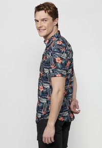 Korte mouwen shirt met een marineblauwe achtergrond, versierd met levendige bloem- en loofpatronen in rood, groen en wit. Met een knoopsluiting bij de kraag, in een ontspannen pasvorm.