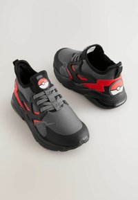 Sorte og røde sneakers lavet af syntetisk materiale, med et Pokéball-design på tungen og siden, samt en tekstureret mellemsål og snørebånd.