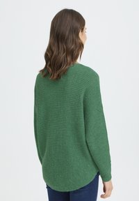 Pull en tricot vert à coupe ample, épaules tombantes et texture côtelée. Il présente un ourlet arrondi et des manches longues.