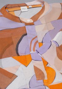 Blouse à manches longues en tissu transparent, présentant un motif abstrait de formes marron, orange et violet. Col boutonné et détail de poche.