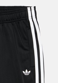 Μαύρο αθλητικό παντελόνι με λευκές ρίγες στα πλάγια, ελαστική μέση και μικρό λευκό λογότυπο αριστερά. Ομαλή υφή υφάσματος.