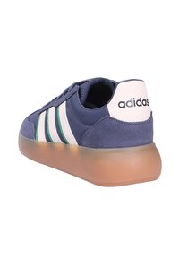 Navy blue Adidas sneaker with white and green stripes, gum rubber sole, suede heel, and white heel tab with black Adidas logo.