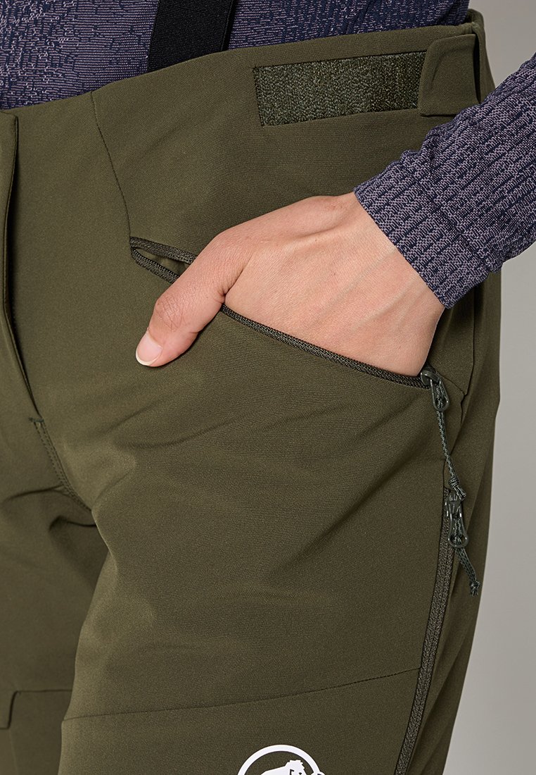 Olivgrüne Hosen mit glatter Textur, ausgestattet mit einer Seitentasche mit Reißverschluss und einem Velcro-Akzent. Ein weißes Logo ist an der unteren Beinpartie sichtbar.