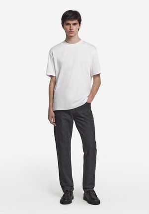 Weißes Kurzarm-T-Shirt kombiniert mit dunkelgrauen geraden Hosen. Das Outfit wird mit schwarzen Sneakers abgerundet. Schlichtes und modernes Design.
