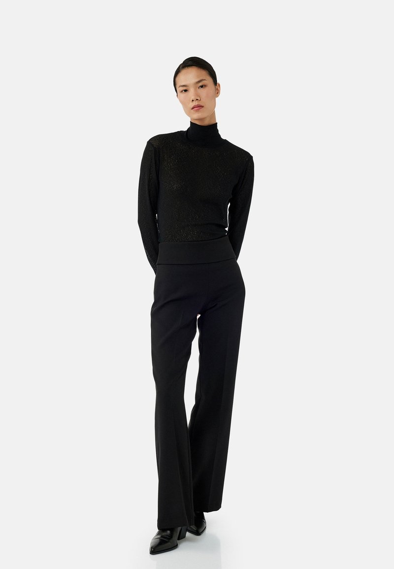 Pull en col roulé noir ajusté avec un motif texturé, associé à un pantalon noir évasé taille haute. Modèle portant des chaussures à talons noires.