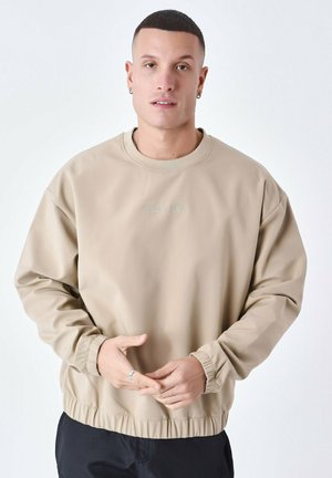Sweatshirt beige en tissu texturé, avec un col rond, des poignets en côte, et un ourlet élastiqué. Logo « Project Paris » en vert clair.