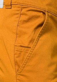 Oranje katoenen broek met een zijzak, gestikte details en een gladde textuur met een lichte glans.