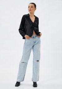 Zwarte satijnen button-up shirt met lange mouwen en een v-hals. Lichtblauwe ripped jeans met een ontspannen pasvorm, gecombineerd met zwarte enkellaarsjes.