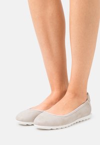Ballerines gris clair avec une tige texturée, semelle blanche flexible, bout rond et col élastiqué pour un ajustement confortable.
