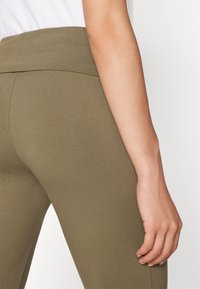 Olive zielone legginsy z wysokim pasem, wykonane z miękkiego, elastycznego materiału. Gładka faktura z szwem biegnącym wzdłuż boku.