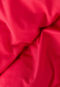 Helles rotes Gewebe mit einer glatten, leicht glänzenden Textur, das weiche Falten und Falten aufweist, was auf ein leichtes oder dehnbares Material hinweist.
