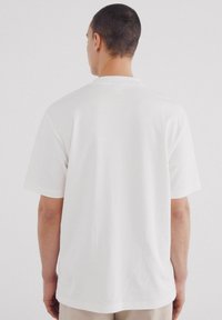 T-shirt bianco a maniche corte, scollatura rotonda, morbido tessuto di cotone con una texture liscia, vestibilità casual, senza decorazioni o motivi visibili.