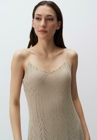 Nude gebreide jurk met een zigzagpatroon, voorzien van dunne verstelbare bandjes en een aansluitende silhout, gemaakt van een lichtgewicht, gestructureerd materiaal.