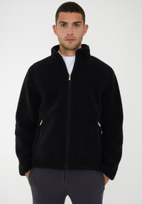 Schwarz gefütterte Jacke mit hohem Kragen, Reißverschluss und Seitentaschen. Verfügt über einen strukturierten Stoff für Wärme und Komfort.