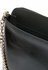 Borsa a tracolla in similpelle nera con una parte superiore curva, finitura testurizzata e tracolla in metallo dorato. L'interno presenta una morbida fodera nera.