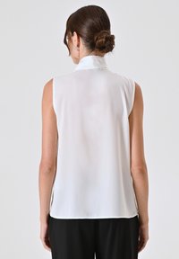 Weiße ärmellose Bluse mit hohem Kragen, glattem Stoff und subtiler Schattierung. Fließt locker und hat einen geraden Saum sowie keine sichtbaren Verschlüsse.