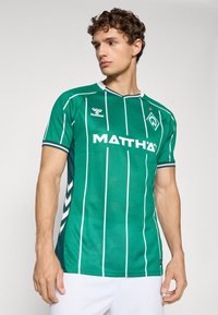 Green soccer jersey with vertical white stripes, short sleeves, textured fabric, and round neckline. Features logo and brand name in white.