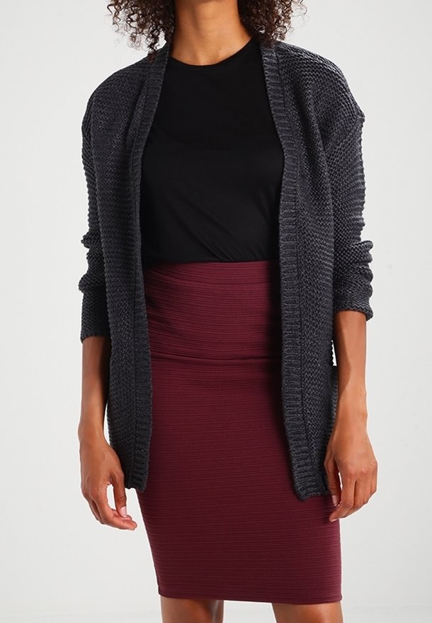 Femme portant un haut noir, un cardigan ouvert en tricot gris foncé et une jupe crayon bordeaux côtelée taille haute.
