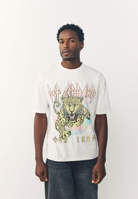 White cotton t-shirt featuring a colorful leopard graphic, "DEF LEPPARD" text, and "OUR 1983" printed in bold yellow text.