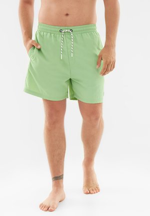 Pantaloni da bagno verde chiaro con cintura elastica, chiusura a cordoncino e tasche laterali, realizzati in tessuto liscio e leggero.