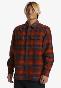 Rød og sort ternet flannel skjorte med blå accenter, knap-op design, to brystlommer og lange ærmer. Blødt, struktureret stof.