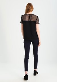 Černý top s průhlednými rukávy s tečkami, vroubkovanými okraji a výřezem na zádech. Nosený s námořnickými skinny kalhotami a černými botami na blokovém podpatku.