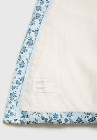 Tessuto bianco morbido con bordi floreali azzurri e un'etichetta cucita con spazi per nome e informazioni telefoniche.