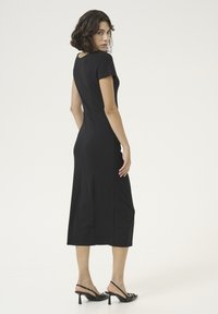 Robe midi noire avec des manches courtes, au design ajusté et avec des fentes latérales. Portée avec des talons slingback noirs, mettant en valeur un tissu lisse et une silhouette épurée.