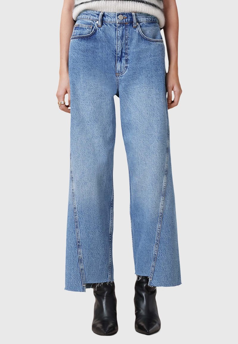 Lysblå brede jeans i denim med høj talje, rå kant og klassisk fem-lommes design. Parret med sorte ankelstøvler.