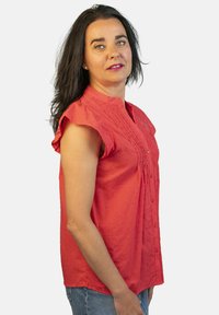 Blusa corta de manga corta roja con cuello mao, que presenta una textura sutil, botones en la parte delantera y detalle de pliegues a lo largo del cuerpo.