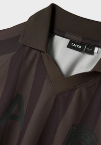 Rudos dryžuotas polo marškinis su V formos apykakle, turintis tekstūruotą audinį ir logotipo detalę kairiajame apačioje. Etiketė matoma viduje apykaklės.