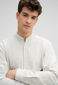Hellgrün und weiß gestreiftes Button-Up-Hemd mit Stehkragen und langen Ärmeln, das über eine subtile Textur und Kunststoffknöpfe verfügt.