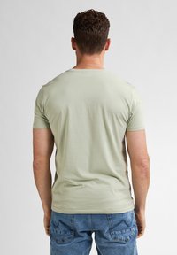 Maglietta verde chiaro a maniche corte realizzata in tessuto morbido. Presenta un collo a giro e un design semplice e aderente.