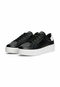 Schwarze Low-Top-Sneaker mit weißen Sohlen, schwarzen Schnürsenkeln und goldenen "Tommy Hilfiger"-Schriftzug an der Seite sowie einem weißen Akzent an der Ferse.